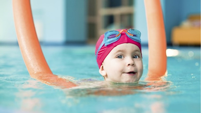 Child using a pool noodle to assist with floatation